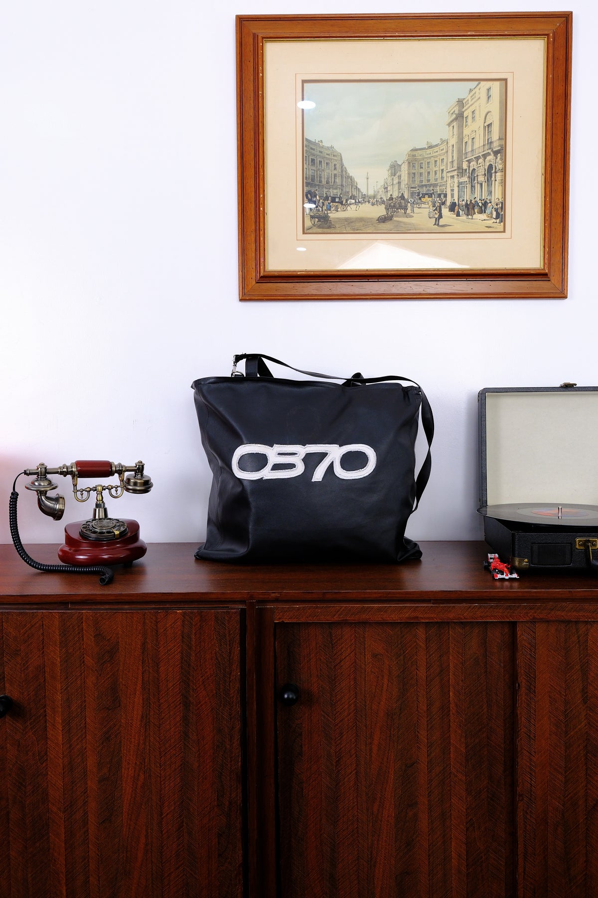 Black bag with '0870' logo on a wooden surface with a framed picture above