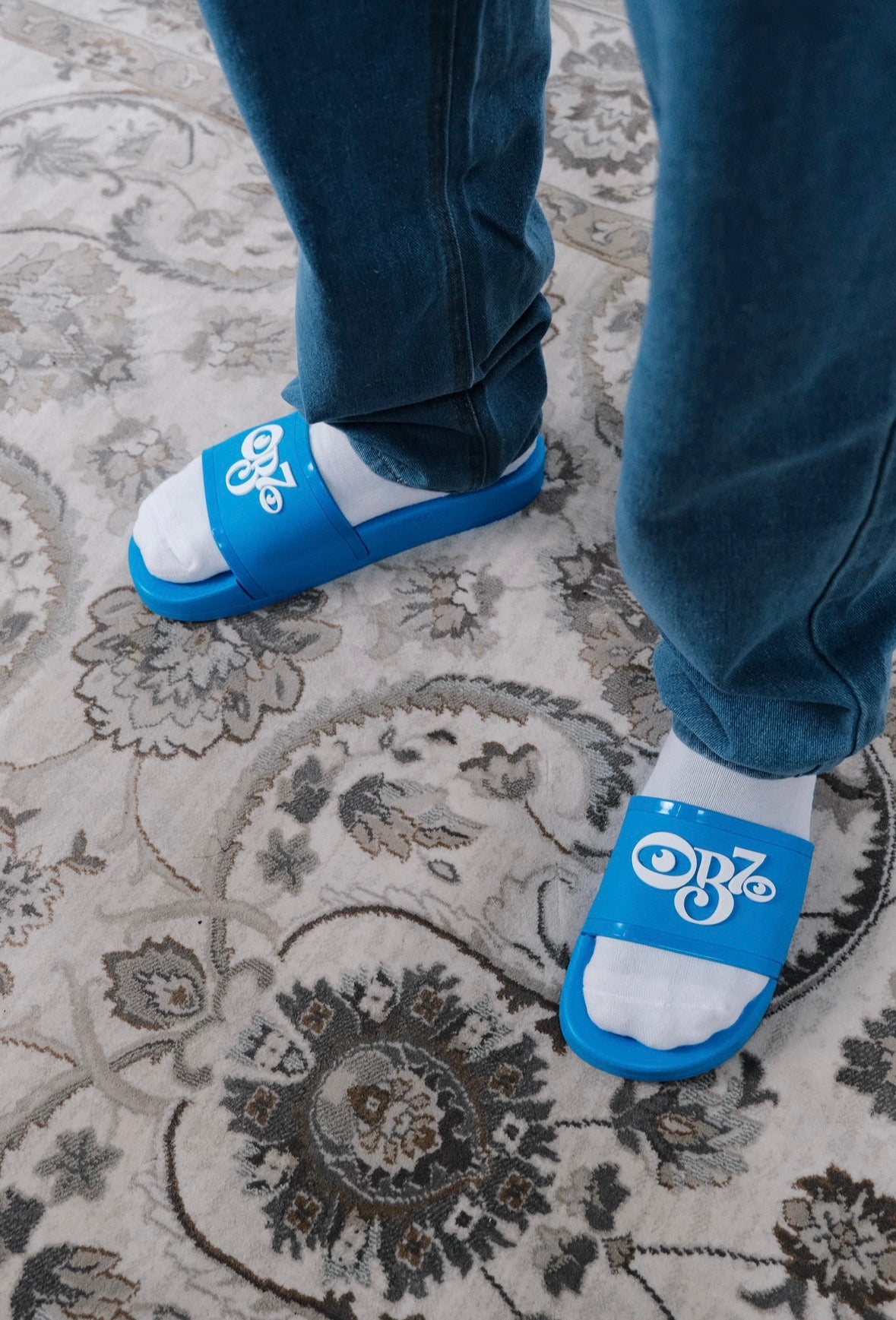 Blue OB70 Classic logo slides with white socks worn on a patterned rug