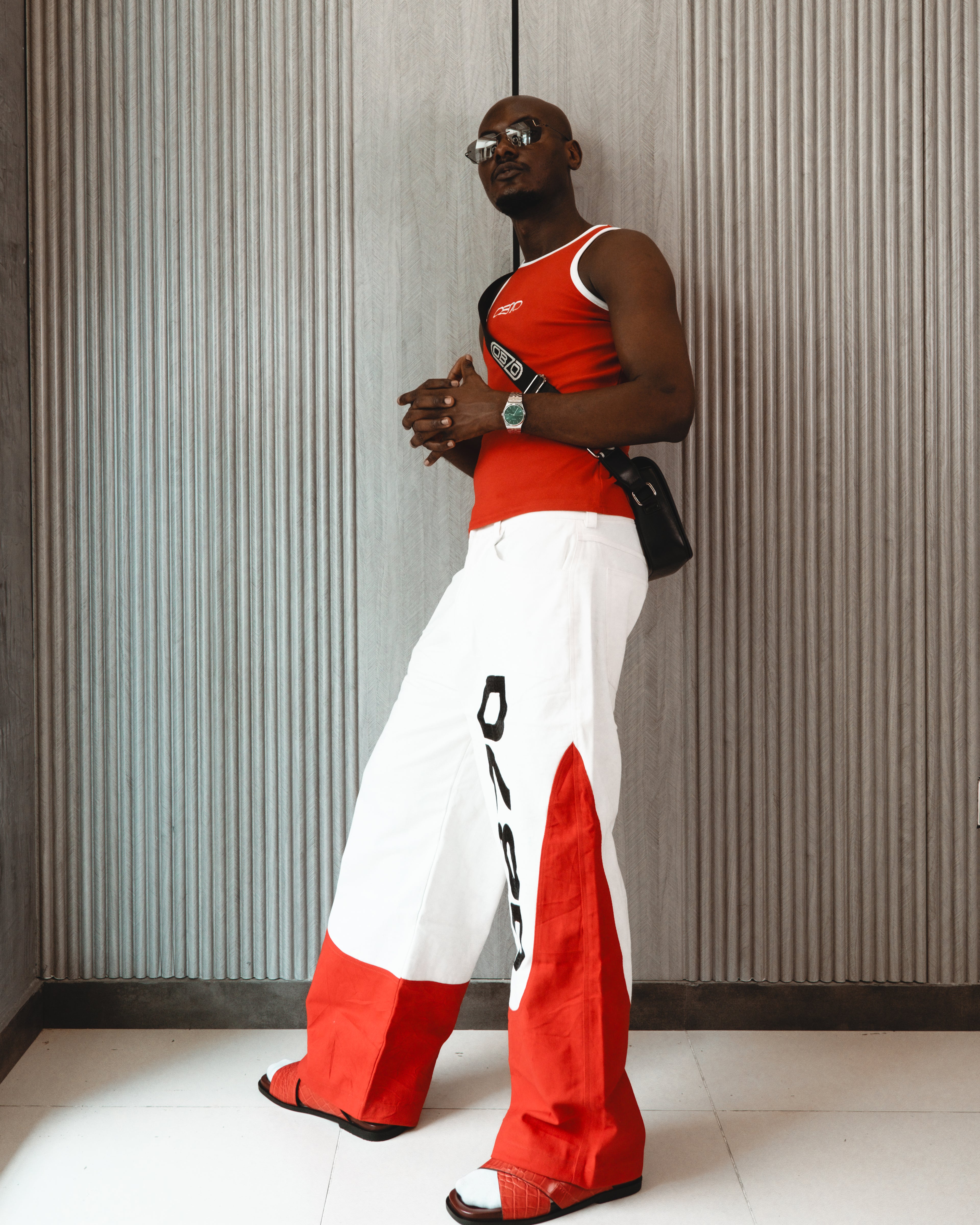 Person wearing a red and white outfit with a black bag against a textured wall.