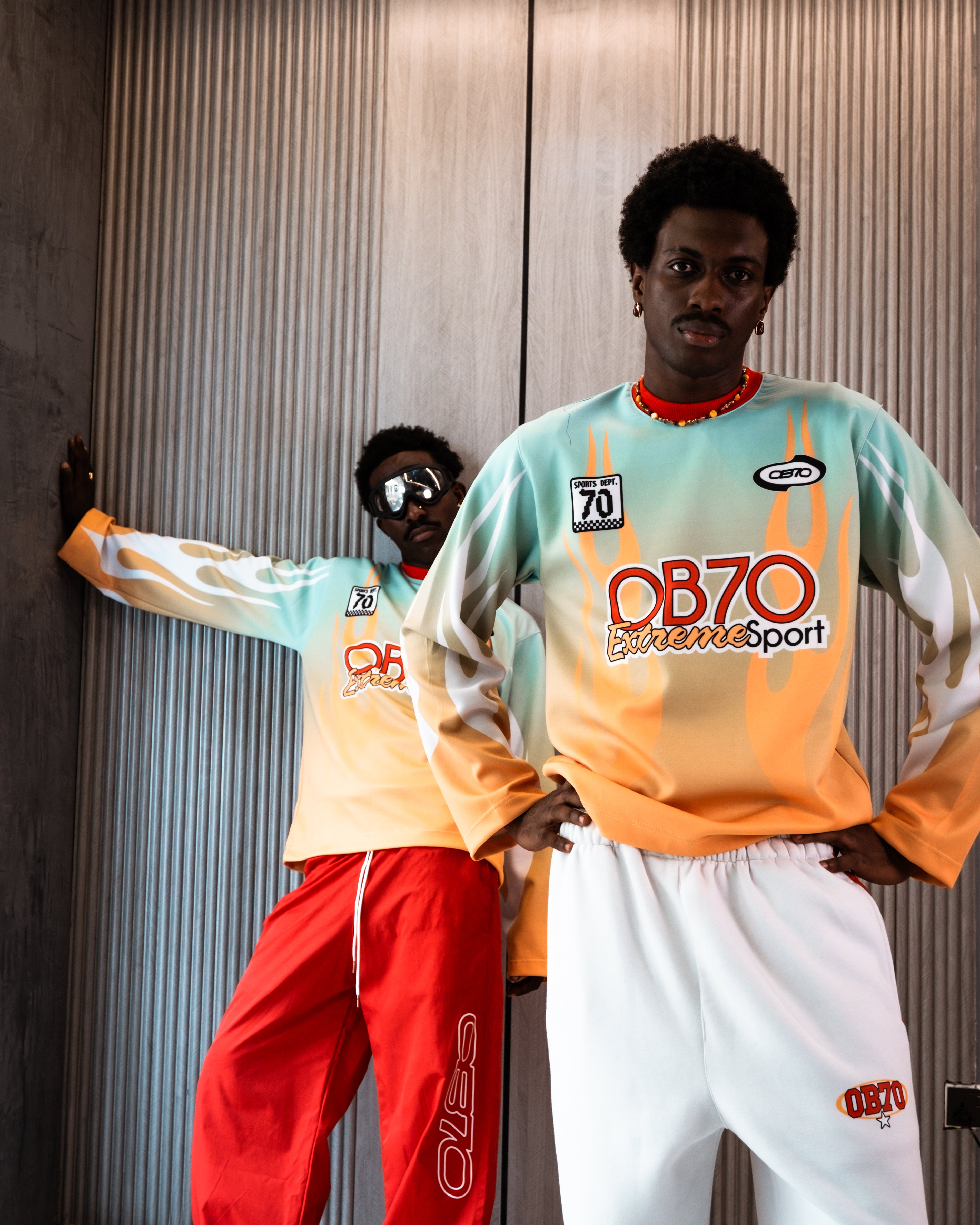 Two people wearing colorful sports outfits with 'OB70 Extreme Sport' branding against a textured wall.