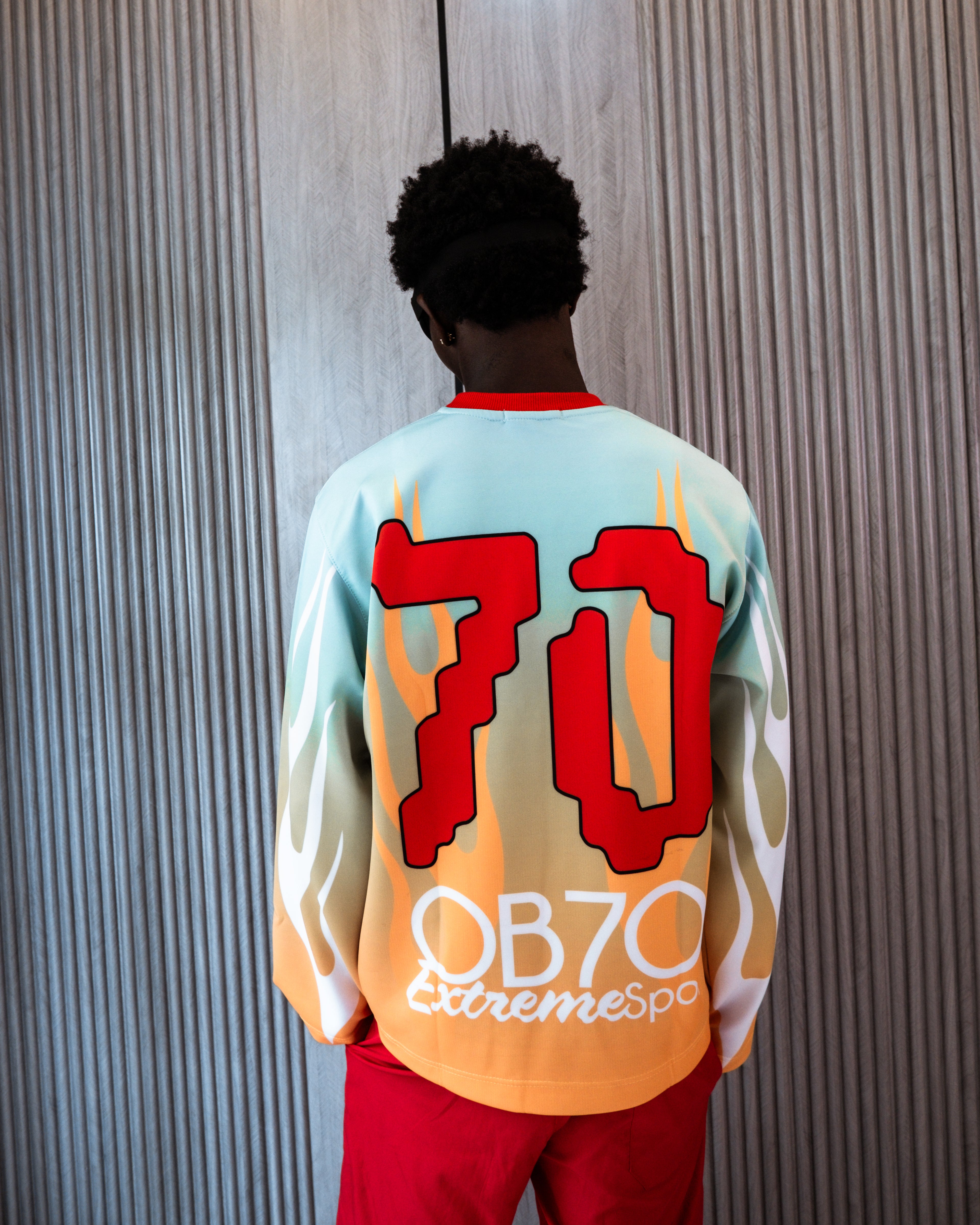 Person wearing a colorful sports jersey with '70 OB70 extremesport' text on the back against a textured wall.