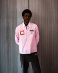 Person wearing a pink shirt with patches against a textured wall