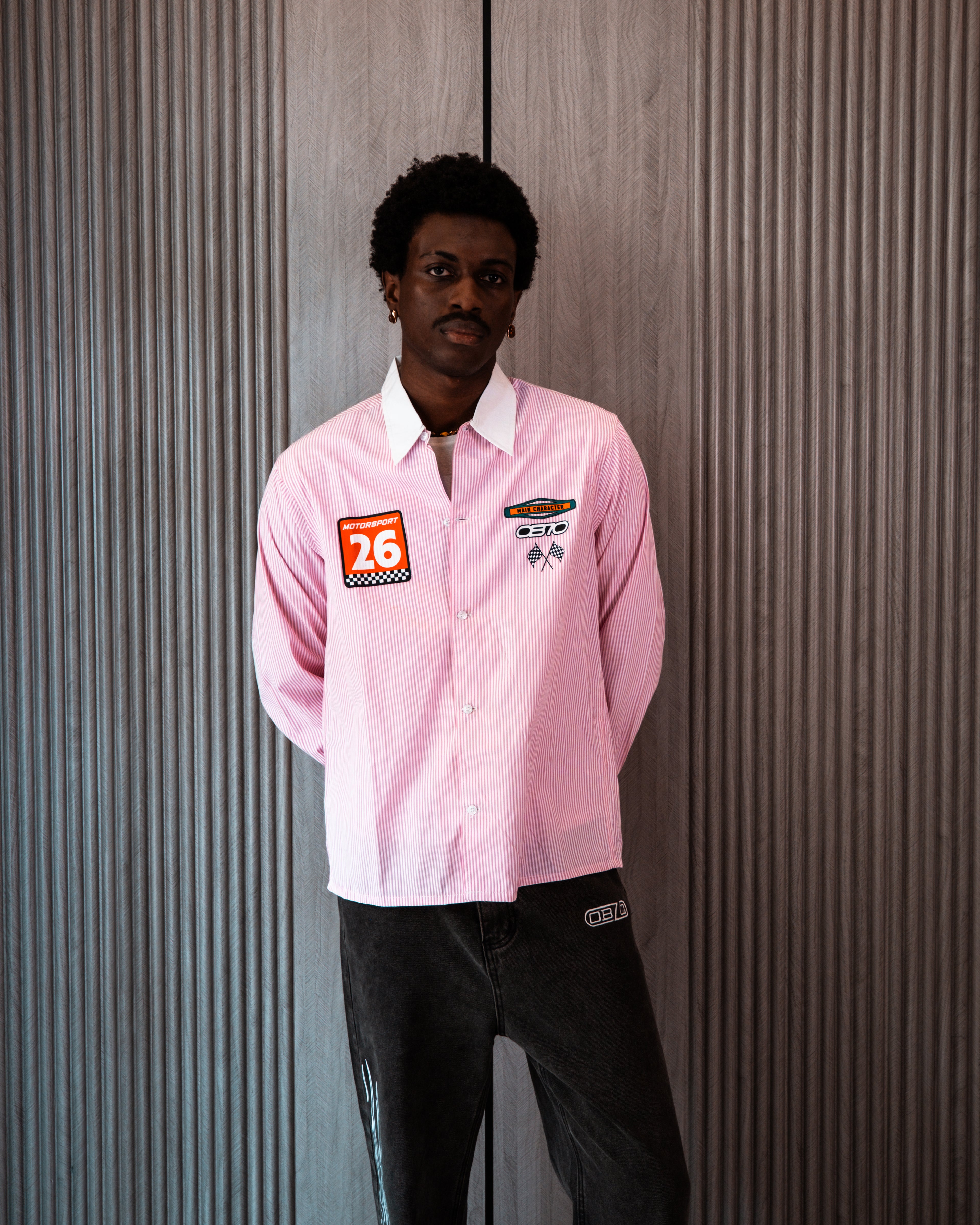 Person wearing a pink shirt with patches against a textured wall